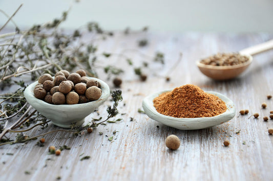 Dried herbs and finely ground powder in ceramic bowls on a rustic wooden table — traditional ingredients often used in Tibetan incense and herbal remedies.
