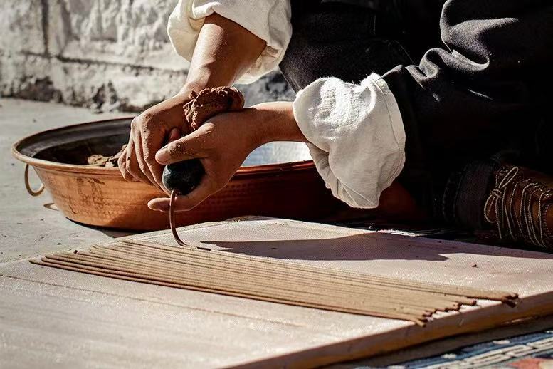 A skilled artisan sitting on the ground, shapes incense sticks on a wooden board, showcasing craftsmanship and attention to detail.