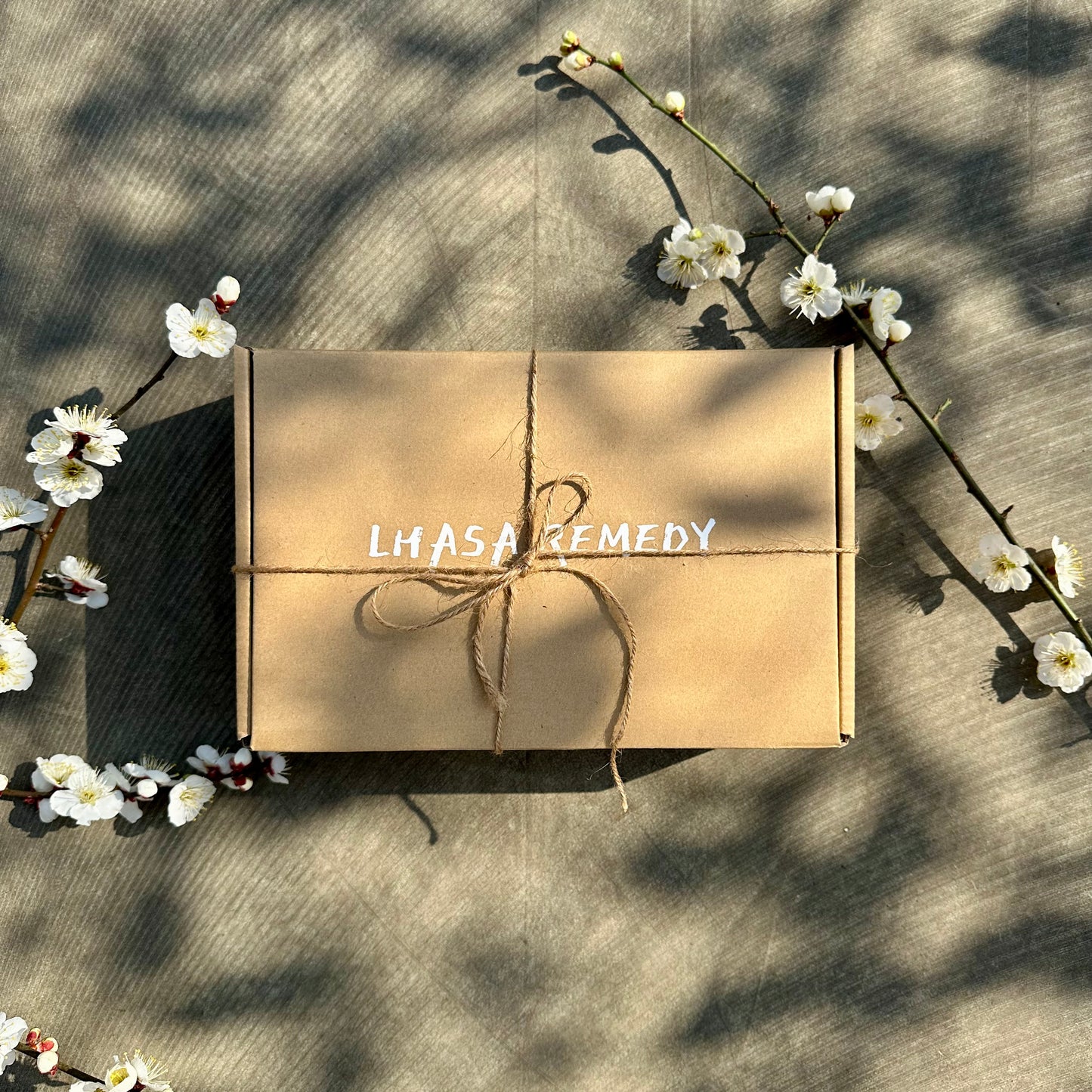 Top view of a Lhasa Remedy product package wrapped with twine, adorned with delicate white flowers, showcasing the brand logo 'Lhasa Remedy' on the brown box.