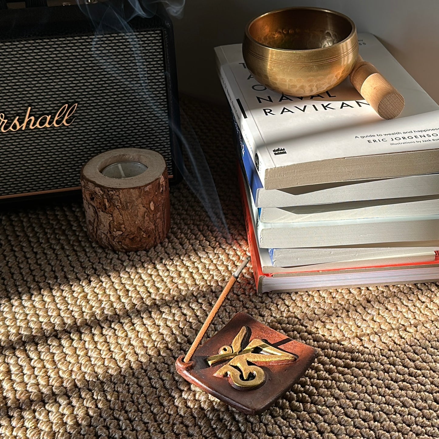 A Chomolung Snow incense stick from Lhasa Remedy burns in a Sacred OM incense holder, with smoke rising beside a stack of books, a brass singing bowl, and a Marshall speaker—creating a warm, reflective ritual space.