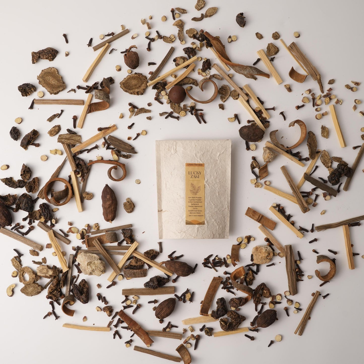 Lucky Zaki Tibetan incense cones by Lhasa Remedy surrounded by a flatlay of traditional Chinese medicine herbs like cardamom, clove, agarwood, and dried roots on a white background.