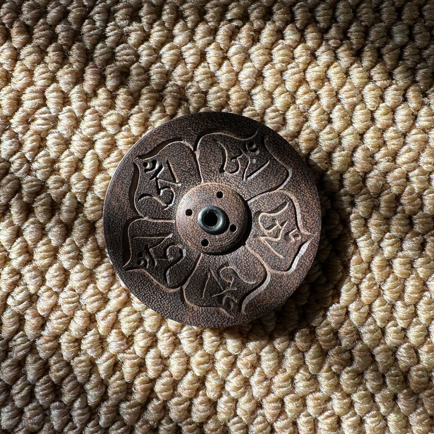 Six Syllable Mantra Wisdom Incense Holder engraved with Om Mani Padme Hum symbols in a circular lotus design, placed on a textured woven mat.