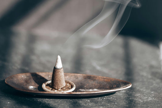 A single incense cone burning on a bronze plate, emitting a gentle aroma in a tranquil setting.
