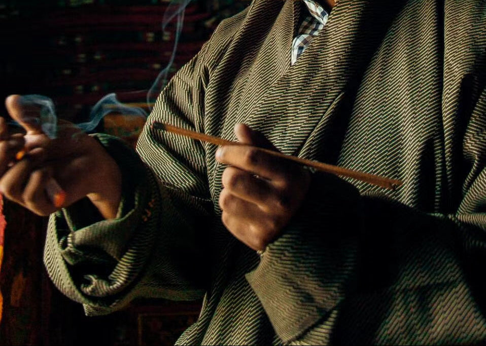 Close-up of a person holding and lighting a handmade Tibetan incense stick as smoke begins to rise.