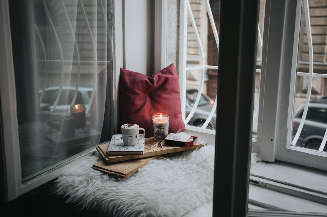 A cozy window nook featuring a lit candle, books, and a warm drink, illustrating why some people prefer candles over incense for relaxation rituals. Highlights the candles vs incense preference in spiritual and daily routines.
