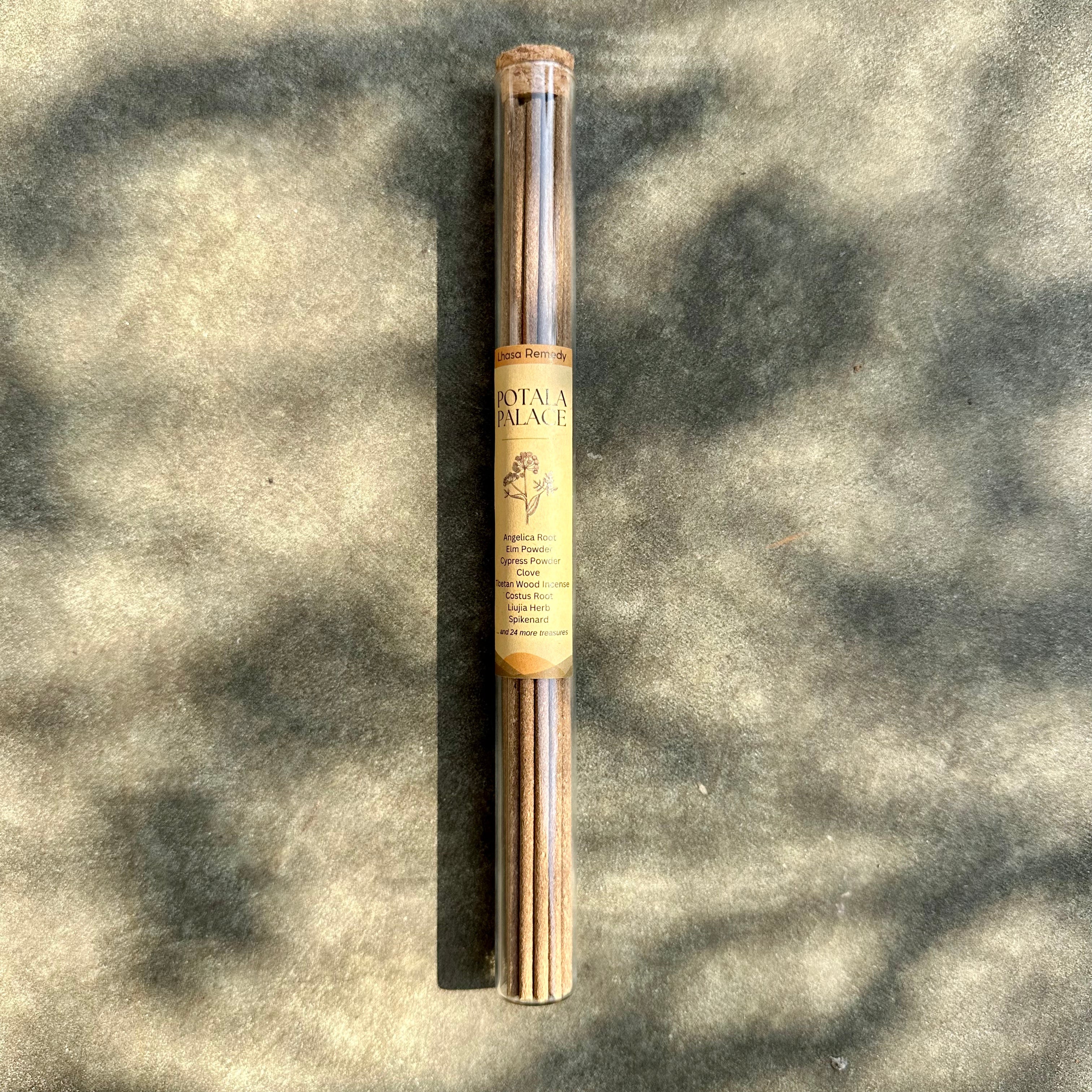 A glass tube positioned on the stone ground, with Tibetan incense sticks in it and a product label of "Potala Palace" sticking onto it, covering by sunshine and shadows.