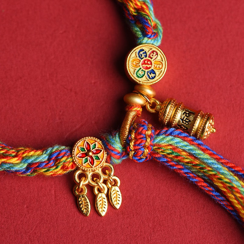 Close-up of Tibetan Prayer Wheel Woven Blessing Bracelet featuring sand-gold prayer wheel charm, Six-Syllable Mantra disc, and dreamcatcher pendant.