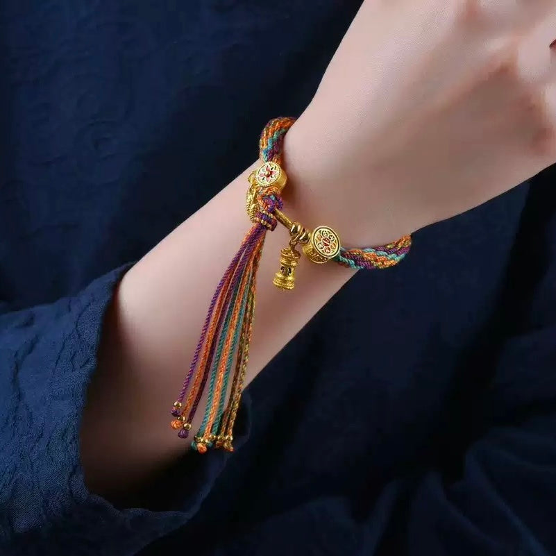 Prayer Wheel Woven Blessing Bracelet worn on wrist, showing gold prayer wheel charm and colorful five-strand braided threads.
