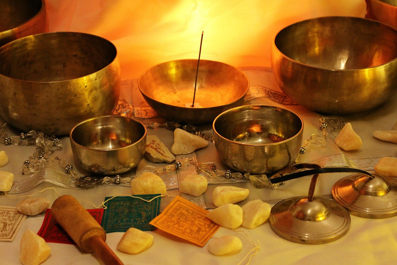 A table adorned with various singing bowls, natural stones, and a glowing incense stick, offering a peaceful and aesthetic ambiance.