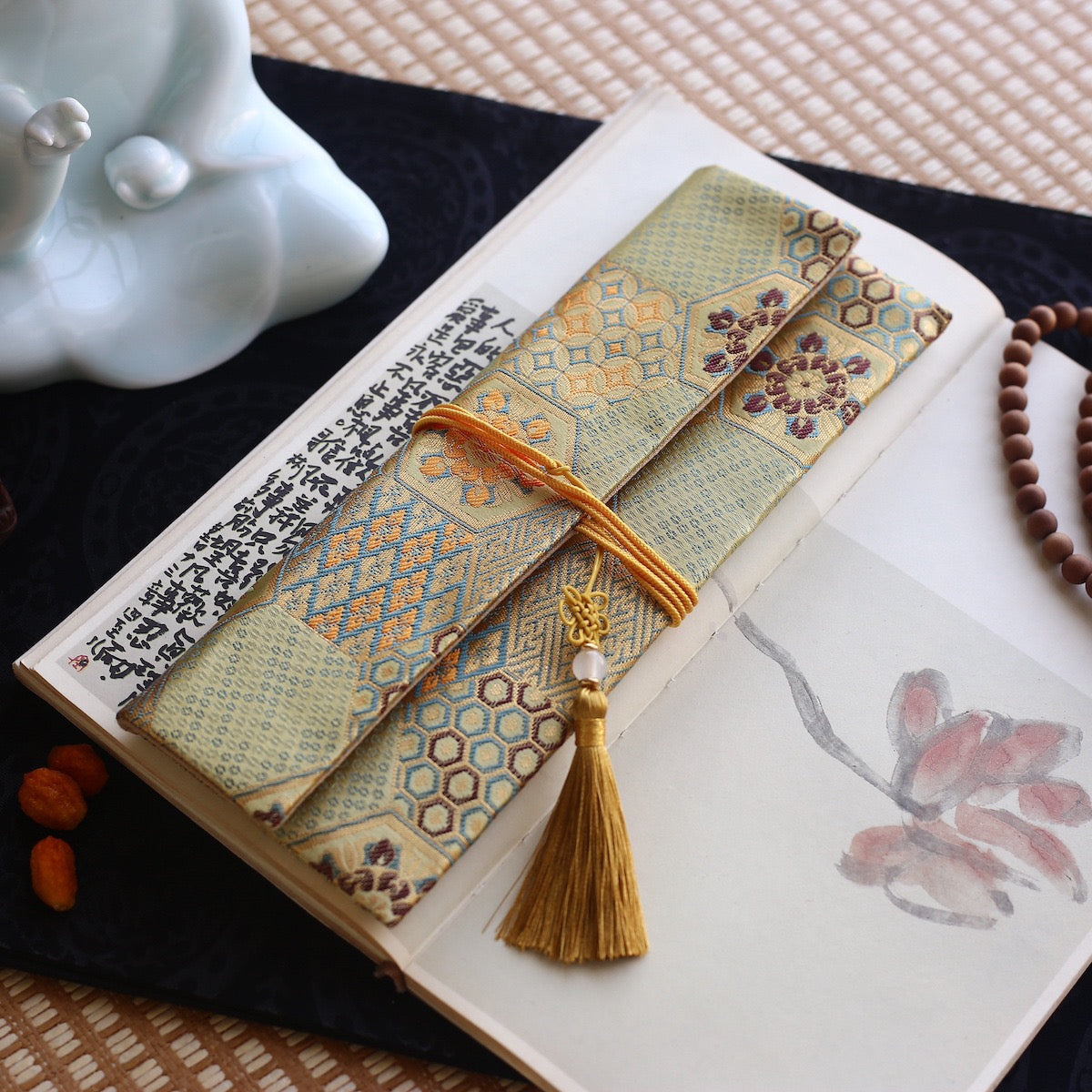 Gold and teal silk incense pouch featuring hexagonal motifs and a golden tassel, resting on a calligraphy book