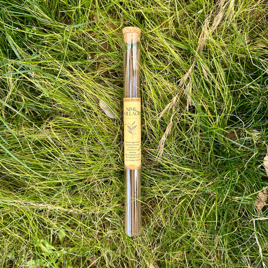 A glass tube of Lhasa Remedy Nimu Village incense sticks with a cork lid, resting on a bed of natural green grass.